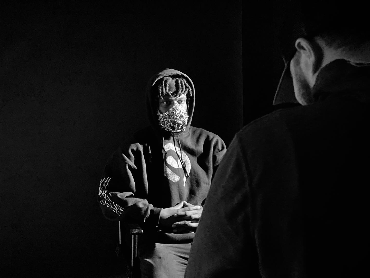 Black and white photo of music artist in a mask sitting in an interview